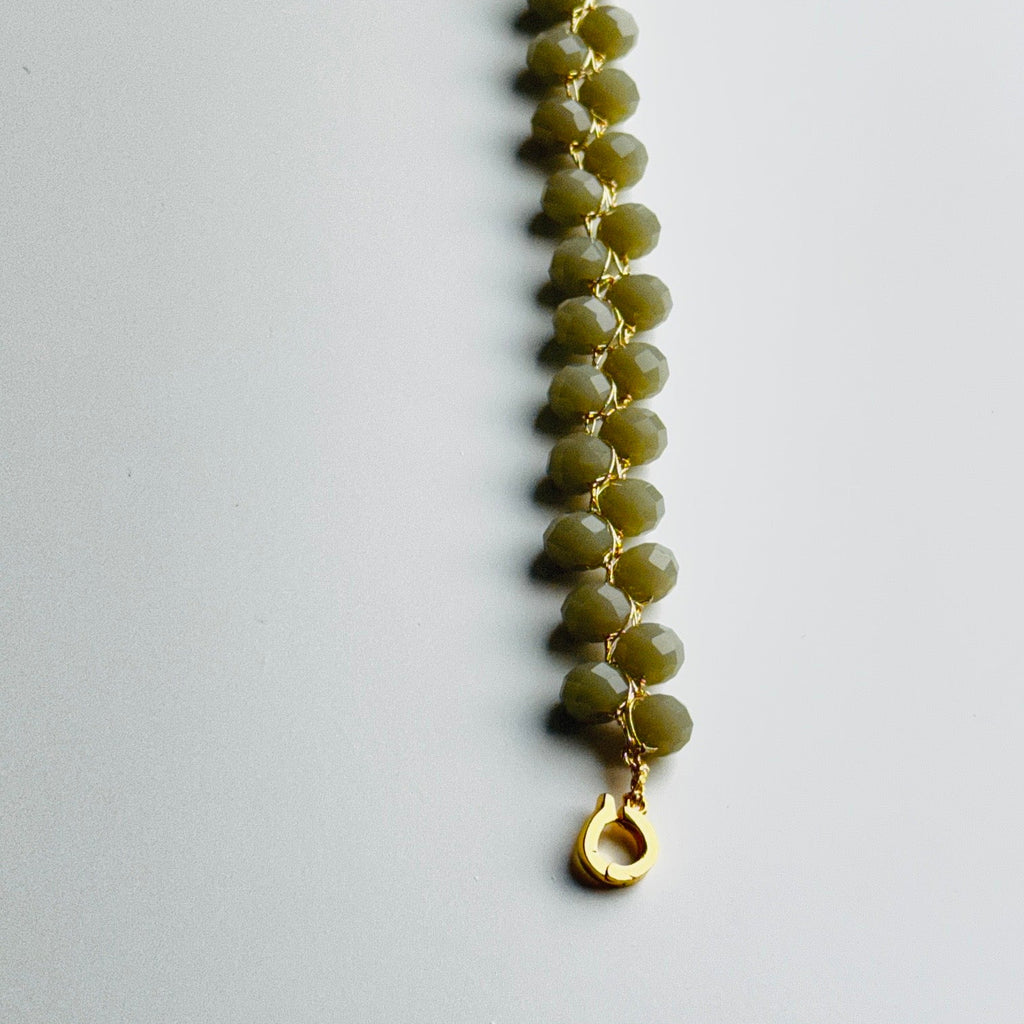 Grey beaded bracelet with a gold clasp on a light gray background