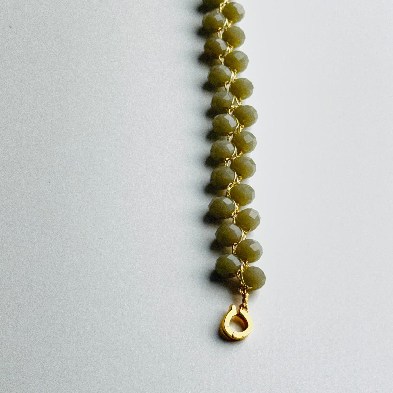 Grey beaded bracelet with a gold clasp on a light gray background
