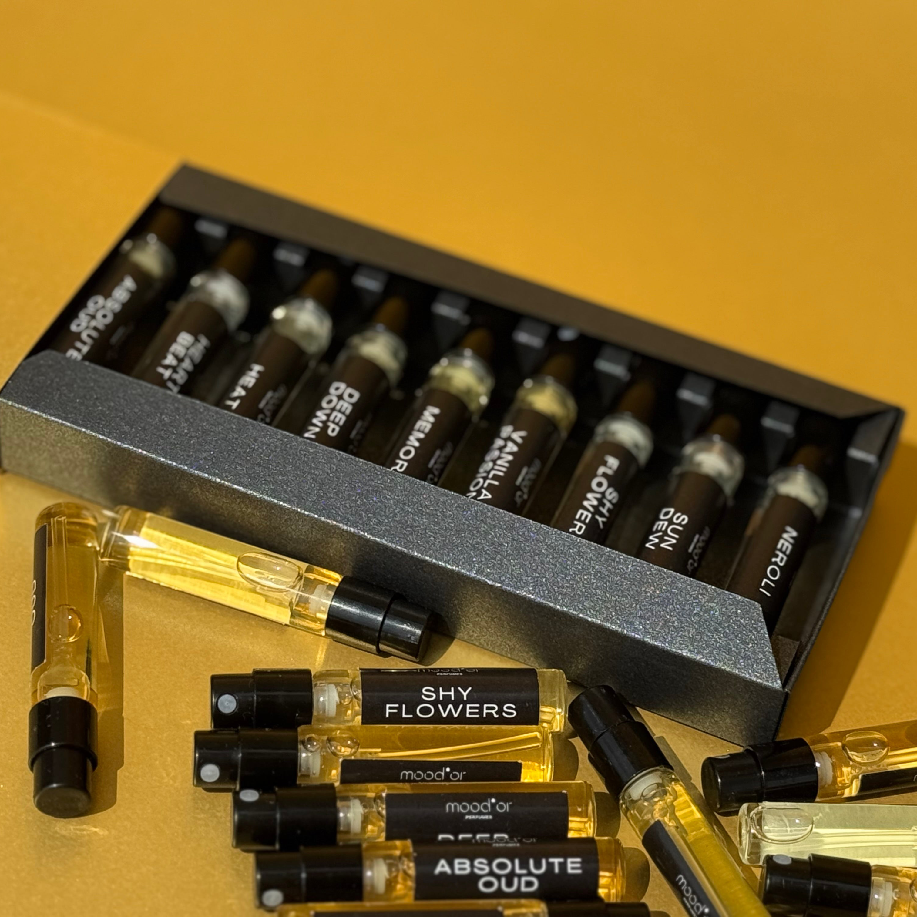 Collection of perfume bottles with visible brand names on a yellow background, Mood'or Perfumes fragrance discovery box