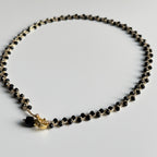 Rankų darbo nerats auksinio atspalvio kaklo papuošalas su juodais stiklo karoliukais