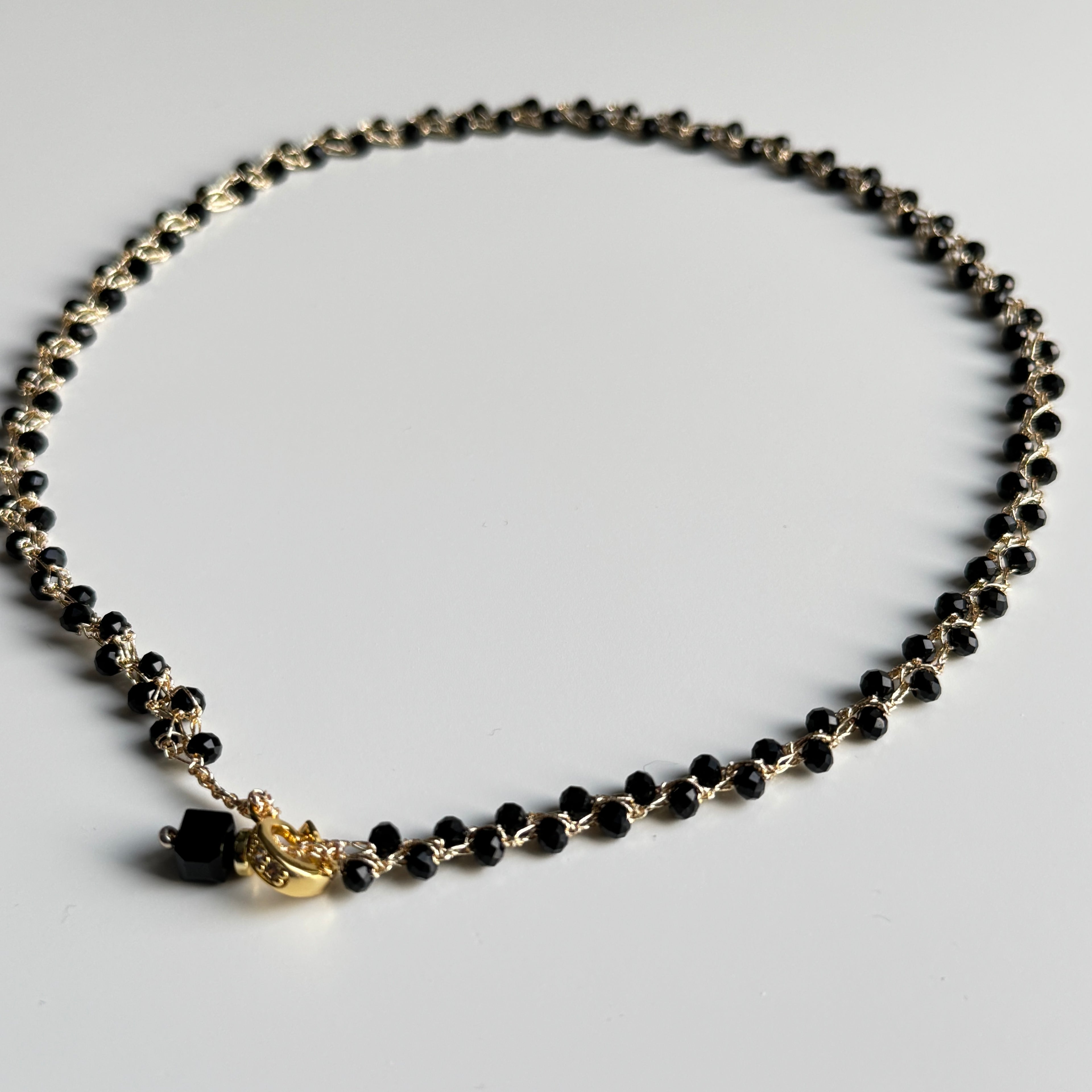 Rankų darbo nerats auksinio atspalvio kaklo papuošalas su juodais stiklo karoliukais