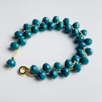 Teal beaded bracelet with gold accents on a light gray background