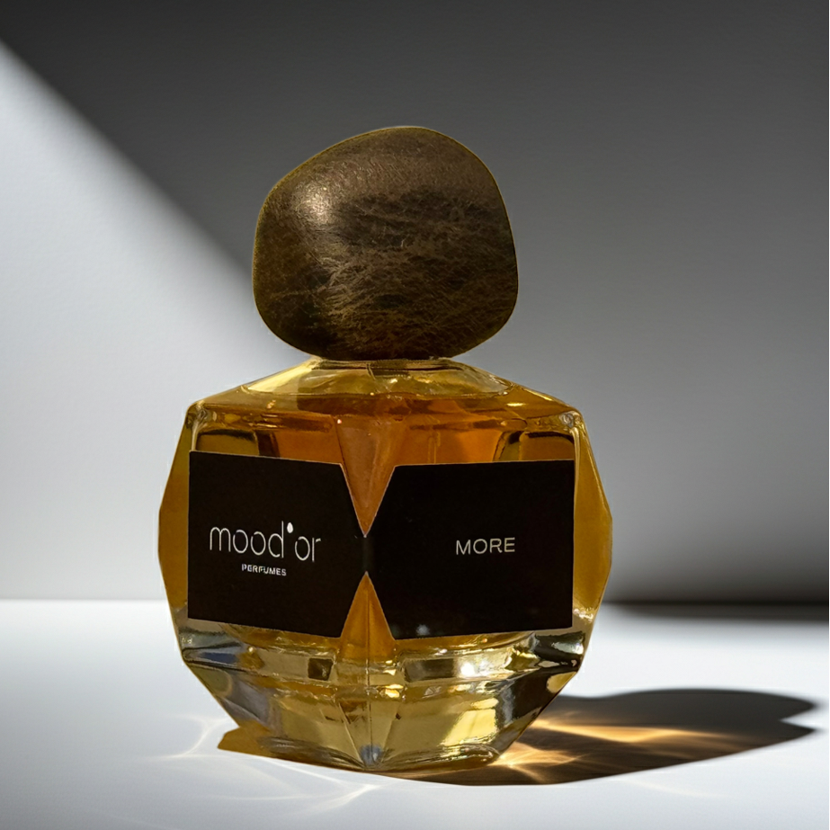 kvepalų buteliukas iš arti su juoda etikete, kurioje užrašas mood'or more